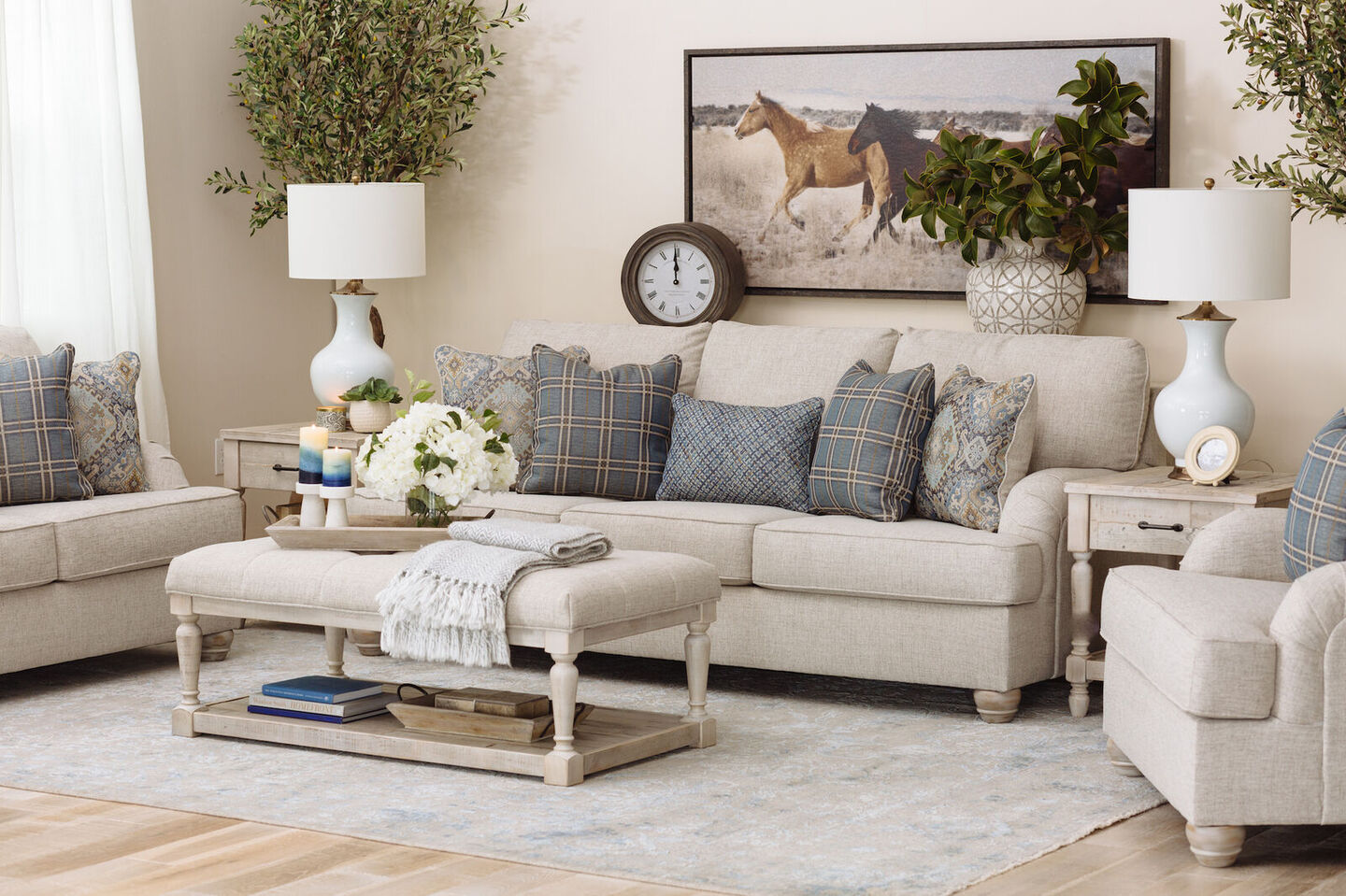 living room with two white lamps, a cream colored couch and a painting of horses hanging above it
